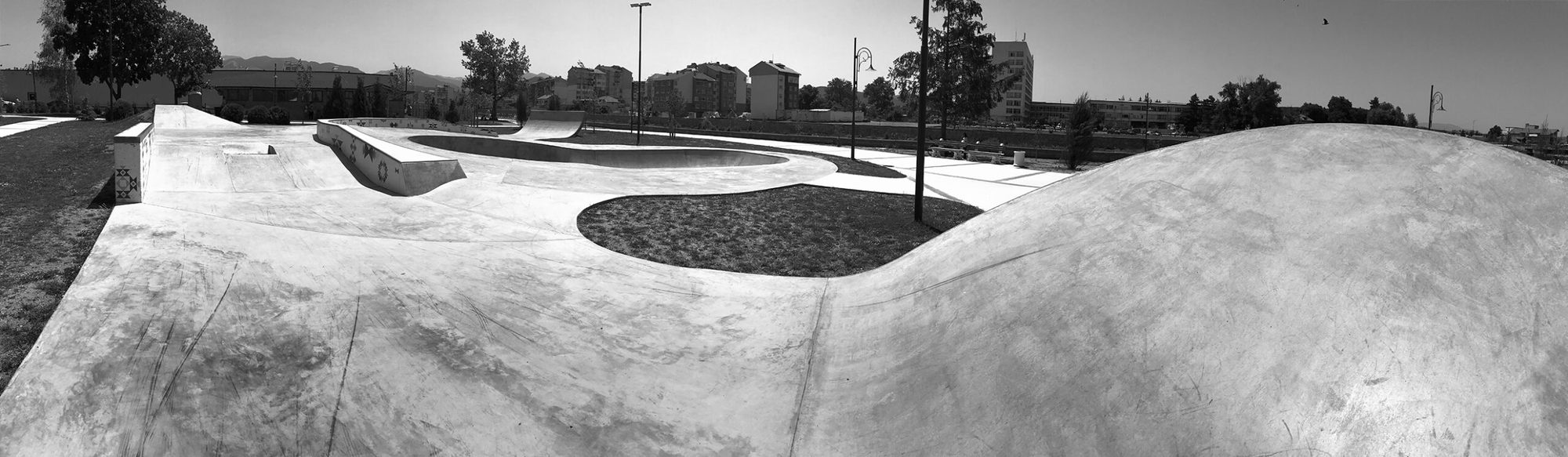 Panorama of a flowing concrete skatepark with rolling hips, ledges and landscaped islands